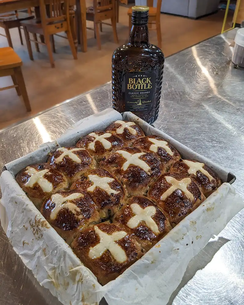 A baking tin contains 12 hot cross buns, glistening with a sticky glaze.