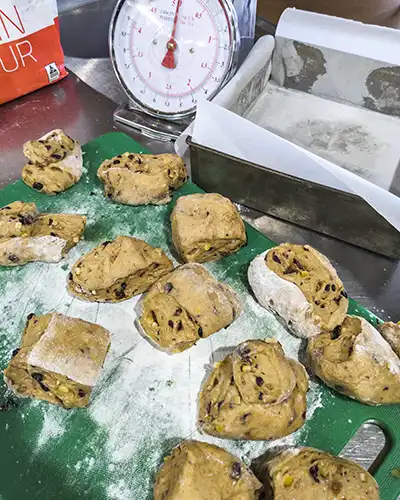 12 100g portions of hot cross bun dough are sitting on a green cutting board.
