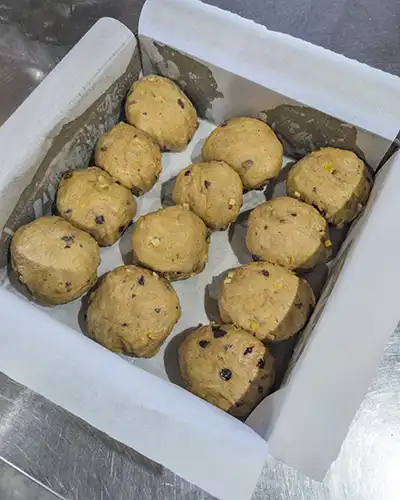12 dough balls are sitting in a square baking tin that has been lined with baking paper.