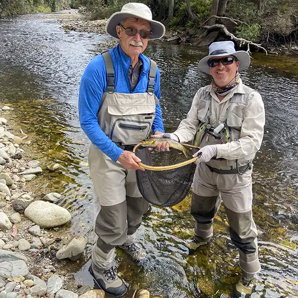Scott Murphy and another man are standing at the edge of a river. They are holding a net and the trout they have just caught.