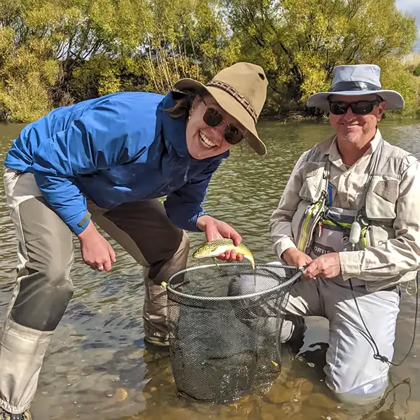Scott Murphy and his guest are at the edge of a river in Tasmania. his guest is holding the trout she just caught,