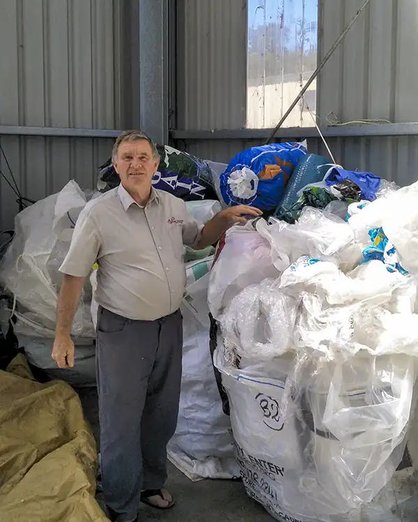 Graham is facing the camera. He has just added a large bag of flexible plastic waste to a pile of bags at the Launceston recycling centre.