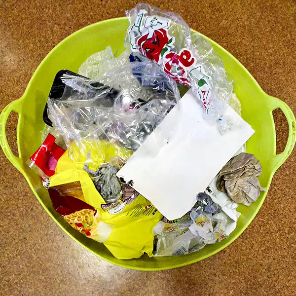A green plastic bin is full to the top with general waste items