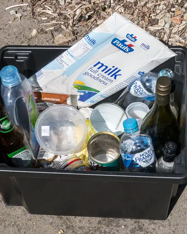 A small black plastic bin is filled with recyclable waste such as glass and plastic bottles.