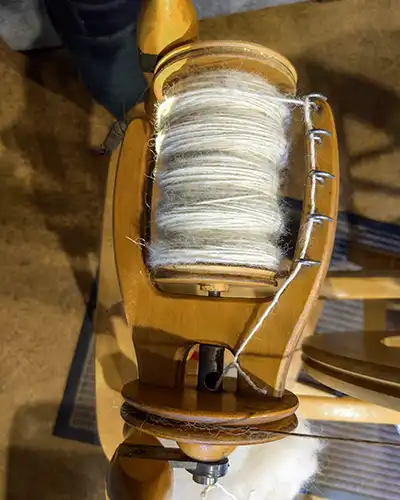 A spinning wheel bobbin is filled with white fibre