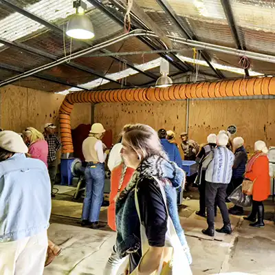 Inside the workshed a group pf people are watching the mini fibre mill in action.
