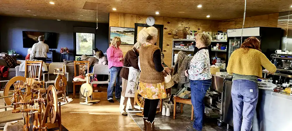 A small group of people are in our barn. They are talking, knitting and spinning.