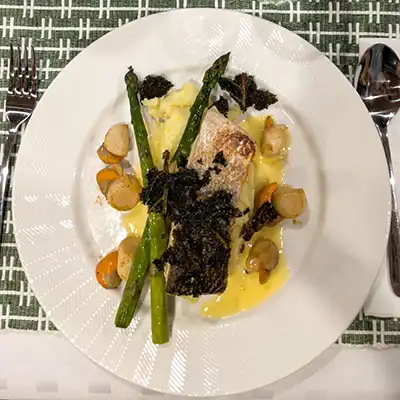 A white meal plate with salmon, scallops, asparagus and baked kale arranged on a pumpkin sauce and potato mash.