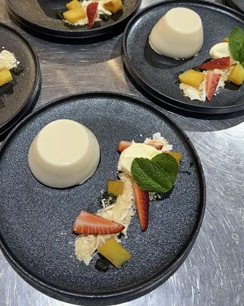 Panna cotta with fresh strawberries and sweet pickled pinapple on a cream sauce with shredded coconut and mint.