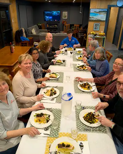 Twelve guests seated a long table with their main course meal in front of them.