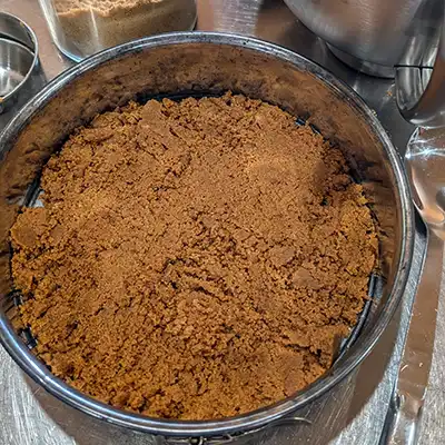 Loose biscuit crumb mix is in the base of a spring-form pan.