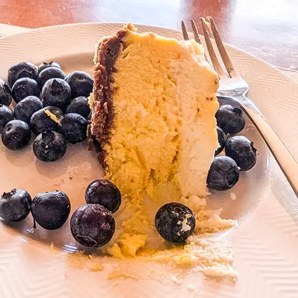 A slice of baked cheesecake with fresh blueberries on a white plate with a cake fork.