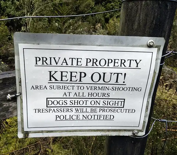 Sign on a fence says Private Property Keep Out! Dogs shot on sight
