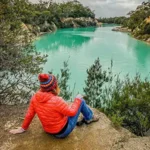 a woman sits facing the Little Blue Lake in North east Tasmania