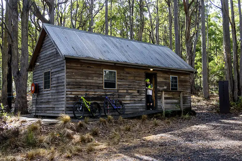 A timber bush hut called the Dettlers Hut at Tin Dragon Cottages in North East Tasmania. Troy Brosnan is standing at the dorr with his mountain bike.